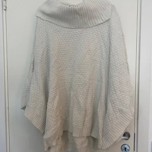 Vit stickad poncho från 365 Sunshine - Mysig vit stickad poncho från 365 Sunshine i storlek M/L. Perfekt för höst och vinter med sitt varma material och stora krage. Den har en fin struktur och ribbade kanter som ger en extra touch. Har legat ett tag i garderob, inte nytvättad. Perfekt att slänga över en tröja för en stilren look! 