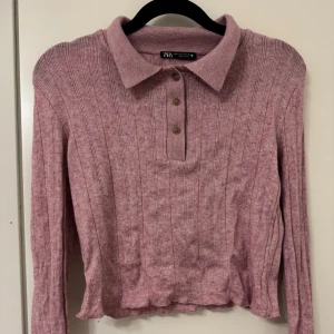 Rosa stickad pikétröja från Zara - Säljer en superfin rosa stickad pikétröja från Zara. Den har långa ärmar och en klassisk krage med tre knappar framtill. Tröjan är i mycket bra skick och har en lätt ribbad struktur. Jag har använt den en gång och säljer då den inte kommer till användning längre.