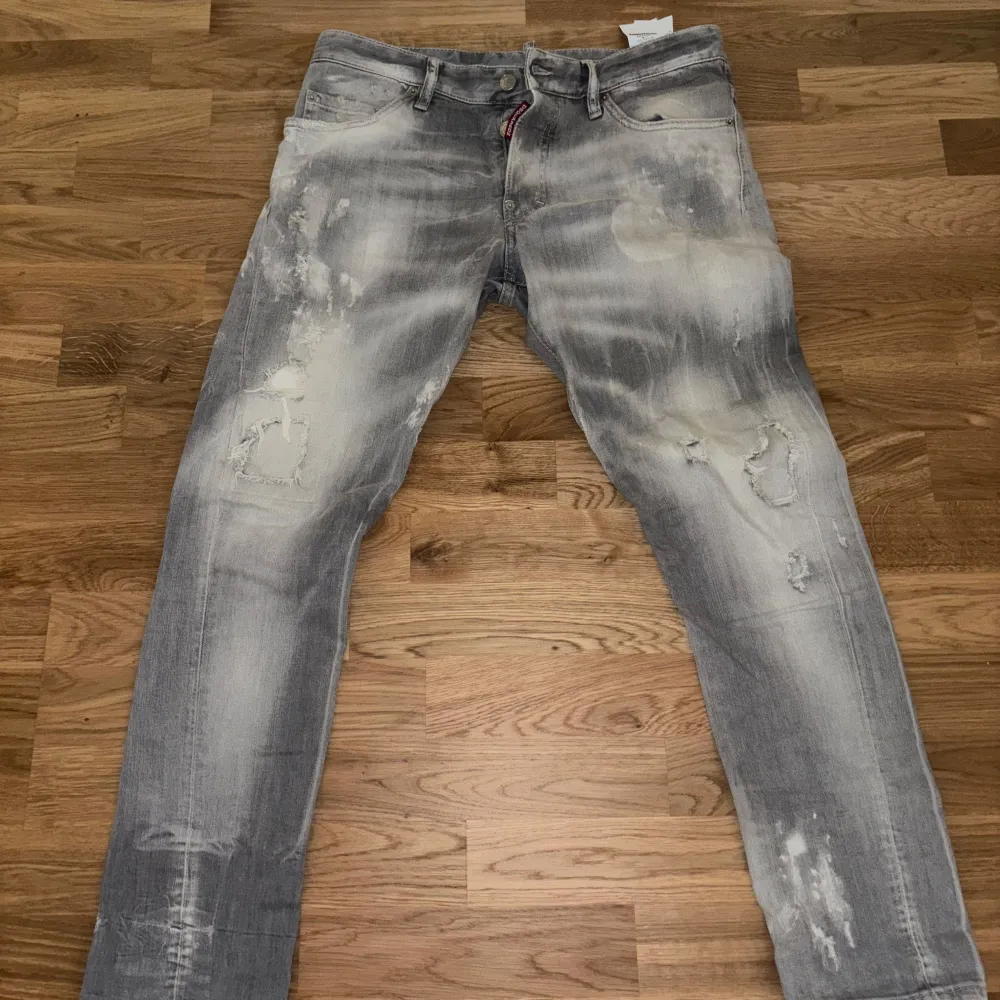 Säljer ett par grå jeans från Dsquared2 i storlek 48. De har en cool, sliten look med ljusa partier och slitningar. Jeansen har knappar och en klassisk femficksdesign. Ny pris runt 3500kr. Kan diskutera om pris. Jeans & Byxor.