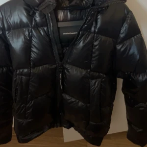 Svart pufferjacka från Peak Performance - Säljer en snygg svart pufferjacka från Peak Performance. Jackan är i mycket bra skick och perfekt för kalla dagar. Den har en dragkedja framtill och en hög krage för extra värme. Passar perfekt för både höst och vinter. Storleken är normal i passformen.
