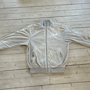 Velour tröja från Corteiz - Säljer en snygg velourtröja från Cortez i storlek M. Jackan har en dragkedja framtill och är tillverkad i ett mjukt material. Den har långa ärmar och ribbade muddar vid ärmslut och nederkant. Perfekt för en avslappnad stil!