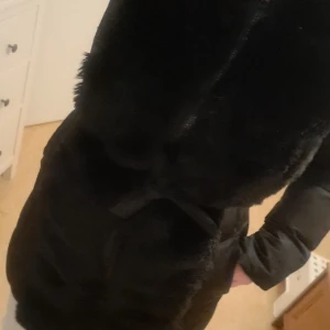 Svart pälsjacka från Brave Soul - Säljer en snygg svart pälsjacka från Brave Soul i storlek S. Jackan har en fluffig pälsdetalj framtill och ett bälte i midjan för en figursydd look. Perfekt för kalla vinterdagar med sin långa ärm och varma design. Passar både till vardags och festliga tillfällen.