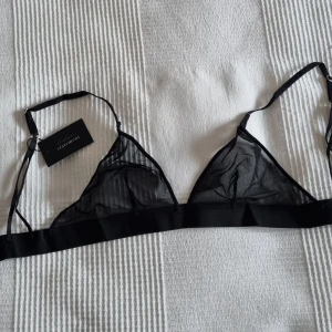 Svart mesh bralette från Understatement - Snygg och stilren svart bralette i mesh från Under statement. Den har justerbara axelband och en enkel design som passar perfekt under en transparent topp eller som den är. Perfekt för en avslappnad och trendig look.