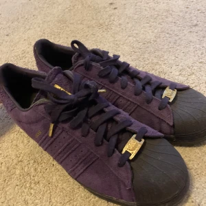 Kaders - Säljer ett par snygga lila Adidas kader i bra skick. De har en klassisk design med snörning och svarta detaljer på tån. Perfekta för både vardag och fest! 🟣