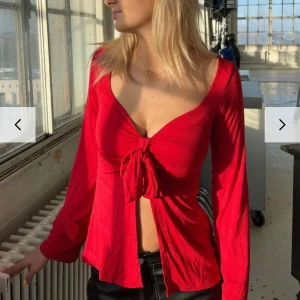 Design by si topp - Snygg röd topp med långa ärmar och knyt framtill. Perfekt för både vardag och fest! Den har en djup v-ringning och är gjord i ett mjukt material som sitter bekvämt. Passar bra till jeans eller kjol. Endast använd några fåtal gånger så väldigt bra skick!