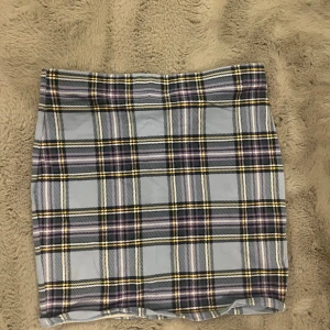 Rutig kjol i blått och gult - Snygg kortkjol med rutigt mönster i blått, gult och svart. Perfekt för en trendig look. Kjolen har en tight passform och är idealisk för både vardag och speciella tillfällen.