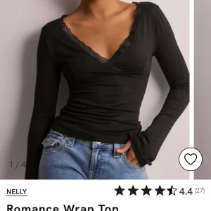 Svart omlottopp från Nelly - Snygg svart omlottopp från Nelly med spetsdetaljer vid halsringningen. Toppen har långa ärmar och en figurnära passform, perfekt för en stilren look. Köptes för 249kr