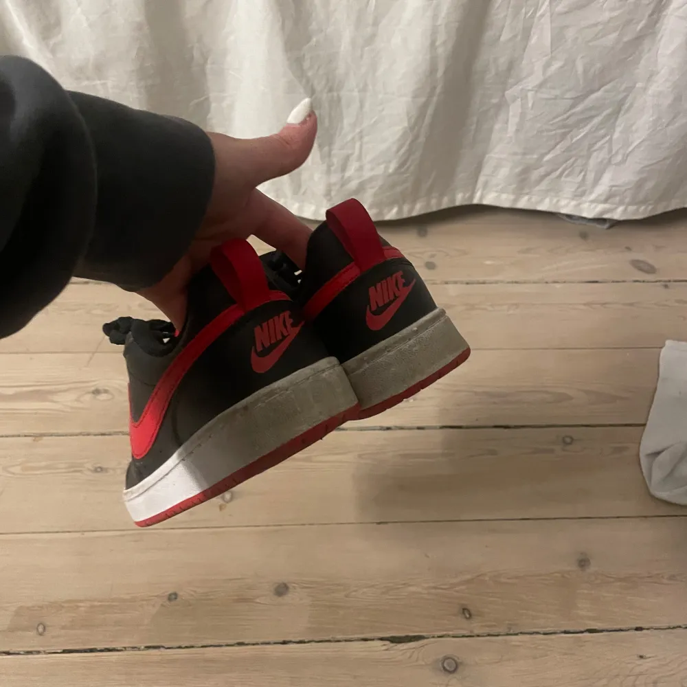 Snygga Nike sneakers i svart och rött med klassisk design. Skorna har en röd Nike-logga på sidan och svart snörning. . Kengät.