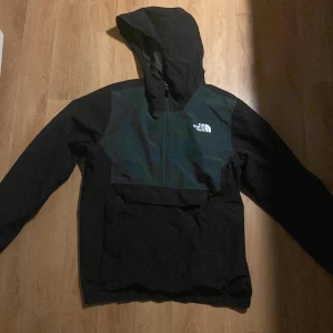 Svart jacka från The North Face - Säljer en svart jacka från The North Face med huva och dragkedja. Jackan har en stilren design med logotypen på bröstet och ryggen. Perfekt för kyligare dagar.