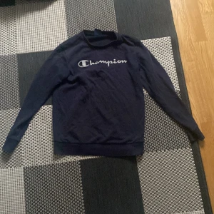 Mörkblå sweatshirt från Champion - Säljer en mörkblå sweatshirt från Champion med deras ikoniska logga på bröstet. Tröjan har långa ärmar och en bekväm passform, perfekt för en avslappnad stil. Tillverkad i mjukt material för extra komfort. Det står att den är X-large men är lika stor som small