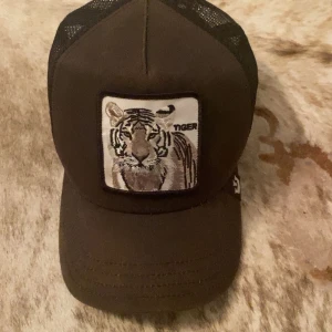  keps - Snygg brun keps med ett coolt tigerbroderi framtill. Kepsen har ett nätmaterial baktill för extra ventilation och komfort. Perfekt för en avslappnad stil.