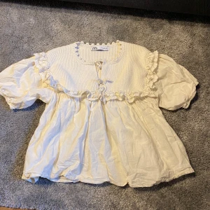 Vit blus med spetsdetaljer från Zara - Charmig vit blus från Zara med puffiga ärmar och vackra spetsdetaljer runt halsen och ärmsluten. Blusen har en lös passform och är perfekt för en romantisk look.