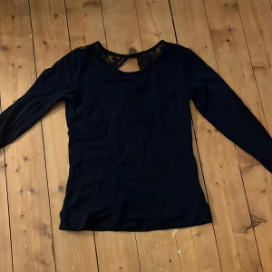 Marin blå långärmad topp med spetsdetaljer - Snygg marin blå långärmad topp med vackra spetsdetaljer vid ryggen. Perfekt för en stilren look. 