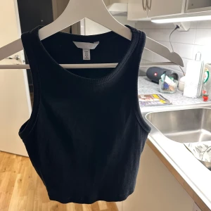 Svart ribbad linnetopp - Snygg svart ribbad linnetopp med ärmlös design. Perfekt för lager-på-lager eller att bära som den är. Enkel och stilren, passar till många olika outfits.