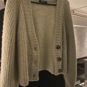 Beige kofta från Gina Tricot - Mysig beige kofta från Gina Tricot med stora knappar framtill. Den har en ribbad struktur och långa ärmar, perfekt för kyliga dagar. En stilren och bekväm tröja att ha i garderoben.