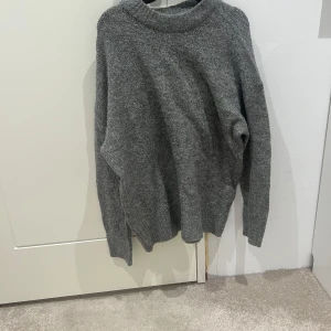 Grå stickad tröja - Mysig grå stickad tröja med långärmad design. Perfekt för kyliga dagar och enkel att matcha med olika outfits.