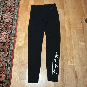 Svarta leggings från Tommy Hilfiger - Snygga svarta leggings från Tommy Hilfiger med vit logga längs benet. Perfekta för en stilren look. Tillverkade i ett stretchigt material för en bekväm passform. Nytt skick, är aldrig använda! PRIS DISKUTERAS!