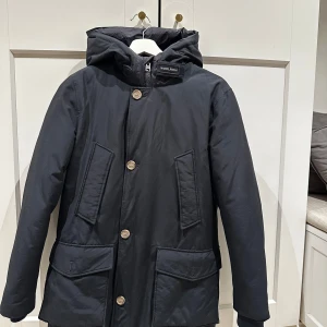 Woolrich Arctic Parka - Säljer en mörkblå parka från Woolrich med huva och knappar. Använd 5-10 gånger. Passar 160-170 cm. Nypris 5000kr