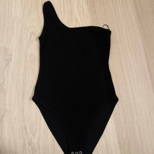 Svart ribbad body - Snygg svart body med en axel och ribbad textur. Använd enstaka gånger, men i jättefint skick. 