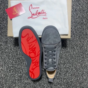 Grå sneakers från loubitash - Snygga grå sneakers i mocka från blish med den ikoniska röda sulan. Skorna har snörning och en stilren design som passar perfekt för en trendig look.