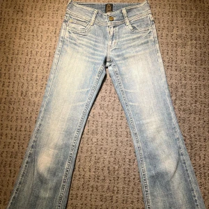 Ljusblå bootcut jeans - Snygga ljusblå bootcut jeans. Jeansen har låg midja och knappar på bakfickorna och är flare. Midja rakt över: 35cm. Lår: 26cm. Innerben: 81cm 