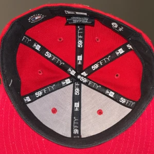 Röd keps från New Era - Snygg röd keps från New Era med New York Yankees-logga i vitt framtill. Kepsen har en klassisk 59FIFTY passform och MLB-logga baktill. Perfekt för sportiga tillfällen eller som en stilren accessoar.