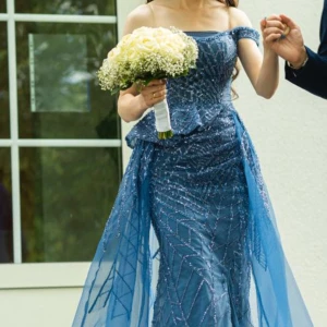 Blå glittrig balklänning - Elegant blå balklänning med glittriga detaljer och offshoulder-design. Klänningen har en vacker omlott-effekt och är perfekt för festliga tillfällen.