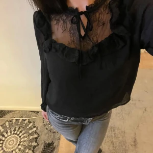 Svart blus med spetsdetaljer - Elegant svart blus med vackra spetsdetaljer och volang vid halsringningen. Blusen har långa ärmar och en knytning framtill, vilket ger en romantisk touch. Classy tröja, aldrig kommit till användning  I strlkn L men passar precis som M och S (jag använder alltid S)  Pris kan diskuteras vid snabbt köp 