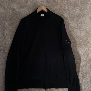 Svart tröja från C.P. Company - Snygg svart tröja  från C.P. Company med dragkedja och ribbad krage. Perfekt för en stilren look.