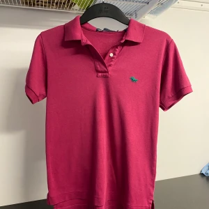 Röd pikétröja från Oscar de la Renta - Snygg röd pikétröja från Oscar de la Renta med klassisk krage och korta ärmar. Tröjan har en liten broderad logga på bröstet och är perfekt för en stilren look. Tillverkad i ett mjukt material för extra komfort.