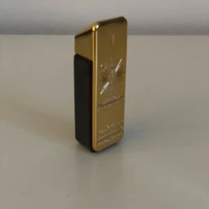 One million parfym sample 4ml/5ml - Elegant parfymflaska i guld med en unik rektangulär design. Flaskan har en dekorativ stjärnliknande gravyr på framsidan och en svart bas. Perfekt för den som vill ha en lyxig touch i sin doftsamling. Rolig liten flaska 4ml av 5 kvar.