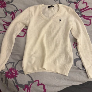 Vit tröja från Ralph Lauren - Säljer en stilren vit tröja från Ralph Lauren med v-ringning. Tröjan har en texturerad yta och långa ärmar. I storlek L, men kan vara mindre i storleken. 