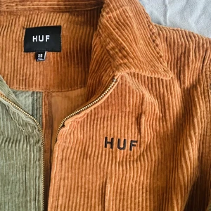 Tvåfärgad manchesterjacka från HUF - Säljer en cool manchesterjacka från HUF i två färger, orange och grön. Jackan har dragkedja framtill och långa ärmar. Perfekt för en avslappnad stil. Helt ny, men lappen är avdragen.