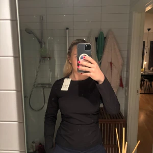 Svart långärmad topp från Zara - Snygg svart långärmad topp från Zara med en tight passform. Perfekt för en stilren look. Toppen har en rund hals och är tillverkad i ett mjukt material.