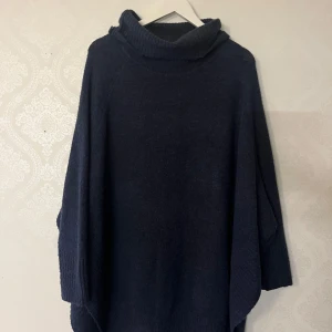 Mörkblå stickad poncho - Säljer en mysig mörkblå stickad poncho med polokrage. Perfekt för kyliga dagar med sin lösa passform och långa ärmar, riktigt stretchig. Ett stilrent plagg som passar till många tillfällen.
