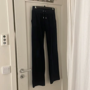 Mörkblå  mjukisbyxor från Juicy Couture - Snygga mörkblå mjukisbyxor från Juicy Couture med hög midja och snörning i midjan. Byxorna har en klassisk design med raka ben och fickor bak. Perfekta för en avslappnad stil.