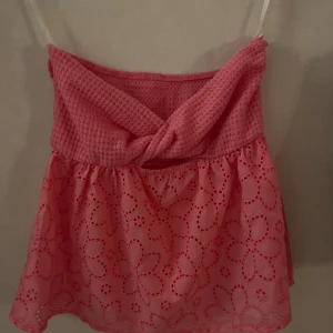 Rosa axelbandslös topp - Söt rosa axelbandslös topp med virkad överdel och blommigt mönster på kjoldelen. Perfekt för sommarens varma dagar.