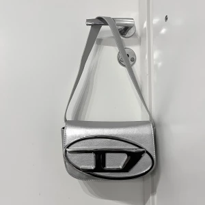 Silverfärgad axelväska med metallogo - ny. säljer pga ej min stil🤍