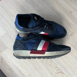 Blå sneakers från Moncler - Snygga blå sneakers från Moncler med detaljer i rött och vitt. Skorna har en kombination av mocka och syntetmaterial samt snörning framtill. Vi har fått dem så tyvärr inte någon originallåda till. Dem har 27,5 cm i innermått. Säljer för 1300kr men kan gå ner i pris vid snabb affär. Kontakta om du har fler frågor. 💗