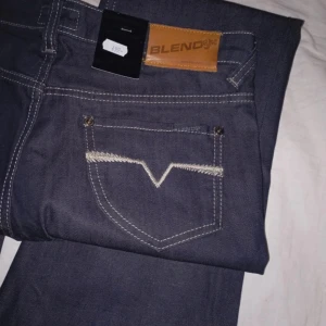 Mörkblå bootcut jeans från Blend - Snygga mörkblå bootcut jeans från Blend med medelmidja och tight passform. Tillverkade i 99% bomull och 1% elastan för en bekväm känsla. Perfekta för en stilren look. Helt nya och oanvända, i storlek 29. Dom är förstora för mig och därför säljer jag dom.