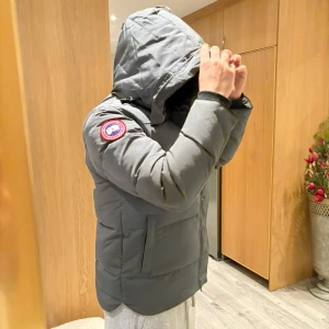 Grå Canada Goose (macmillan) - Säljer en stilren grå dunjacka från Canada Goose med huva och ikonisk logga på ärmen. Jackan har dragkedja och knappar framtill för extra skydd mot kyla. Perfekt för kalla vinterdagar. En byteliten defekt vid sista bilden men inget man tänker på annars är den i nyskick och endast använd 10 gånger , tagsen medföljer också. 