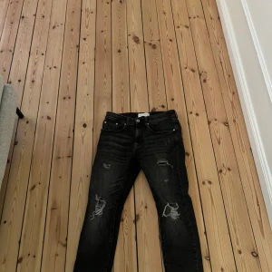 Svarta jeans med slitningar - Snygga svarta jeans med coola slitningar på framsidan. Perfekta för en avslappnad stil. Har en slim fit. Använda endast några fåtal gånger.