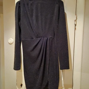 Svart glittrig klänning från Shein - Snygg svart klänning från Shein med glittrigt material och draperad detalj framtill. Klänningen har långa ärmar och en elegant passform som passar perfekt för festliga tillfällen.