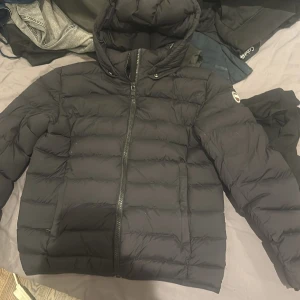 Svart dunjacka från Colmar - Säljer en svart dunjacka från Colmar med huva och dragkedja. Jackan har en stilren design med Colmar-logga på ärmen och baktill.  Väldigt bra skick, kan diskutera pris!