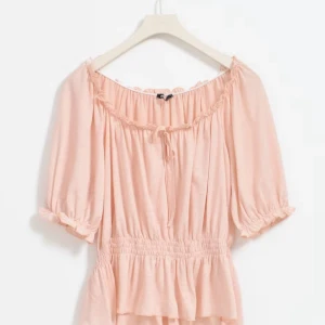 Ljusrosa blus med resårdetaljer - Charmig ljusrosa blus med resår i midjan och vid ärmslut. Blusen har en söt knytning vid halsen och korta puffärmar som ger en romantisk touch. Aldrig använd, köpte för 299💗