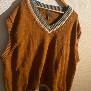 Orange stickad väst från H&M - Säljer en snygg orange stickad väst från H&M med v-ringad krage i blått och vitt. Perfekt för lager-på-lager-stil och ger en trendig touch till din outfit.