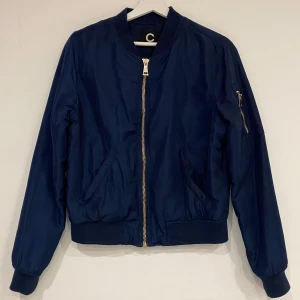 Mörkblå bomberjacka - Snygg mörkblå bomberjacka med guldiga dragkedjor. Storlek S