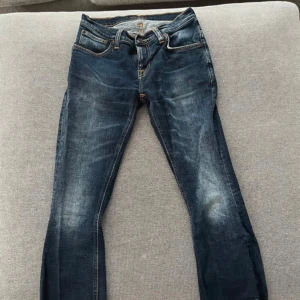 Mörkblå jeans från Nudie Jeans - Snygga mörkblå jeans från Nudie Jeans med klassisk femficksdesign och orange sömmar. Jeansen har en sliten look med fransiga benslut och en bekväm passform. Perfekta för en avslappnad stil. Nya kostar runt 2000kr. 