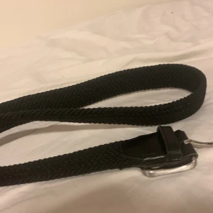 Svart flätat bälte - Snyggt svart flätat bälte med en stilren silverfärgad spänne. Perfekt för att ge en extra touch till din outfit. Passar till både jeans och kostymbyxor.