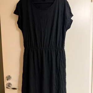 Svart klänning från Gina Tricot - Snygg svart klänning från Gina Tricot i en enkel och stilren design. Klänningen har korta ärmar och en normal passform, perfekt för olika tillfällen. Tillverkad i ett bekvämt material som ger en skön känsla.